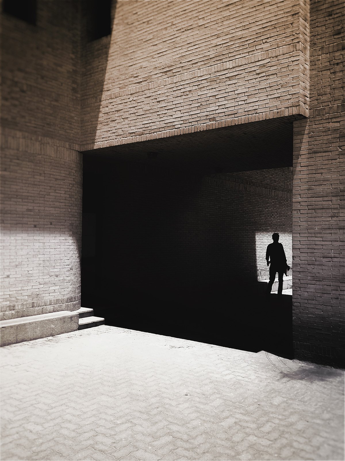 Minimalist street photography from the 'Urban Eclipse' series, featuring silhouettes and sharp geometric shadows against urban brick architecture.
