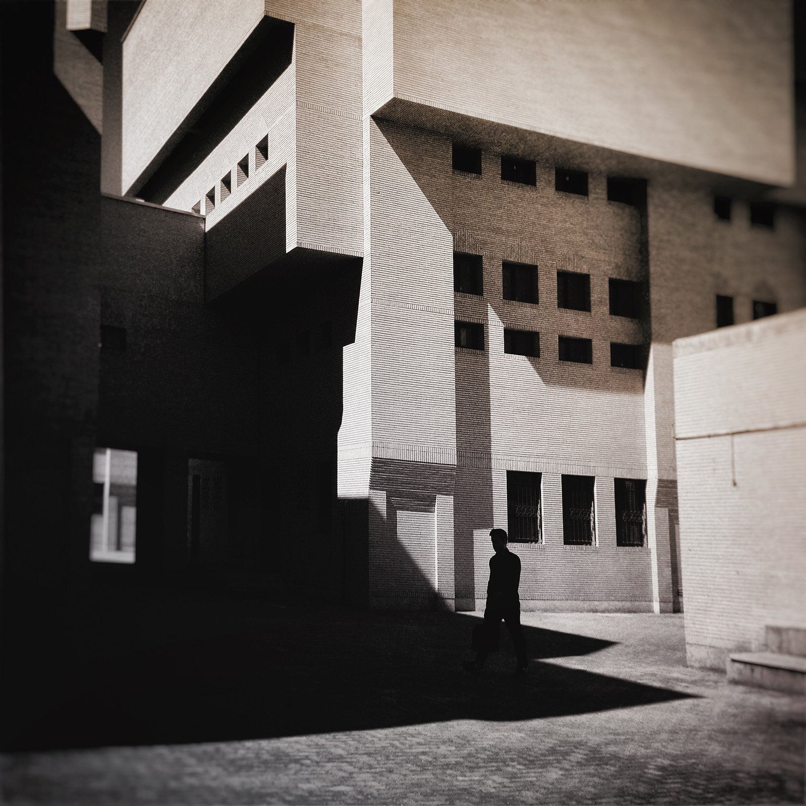 Minimalist street photography from the 'Urban Eclipse' series, featuring silhouettes and sharp geometric shadows against urban brick architecture.