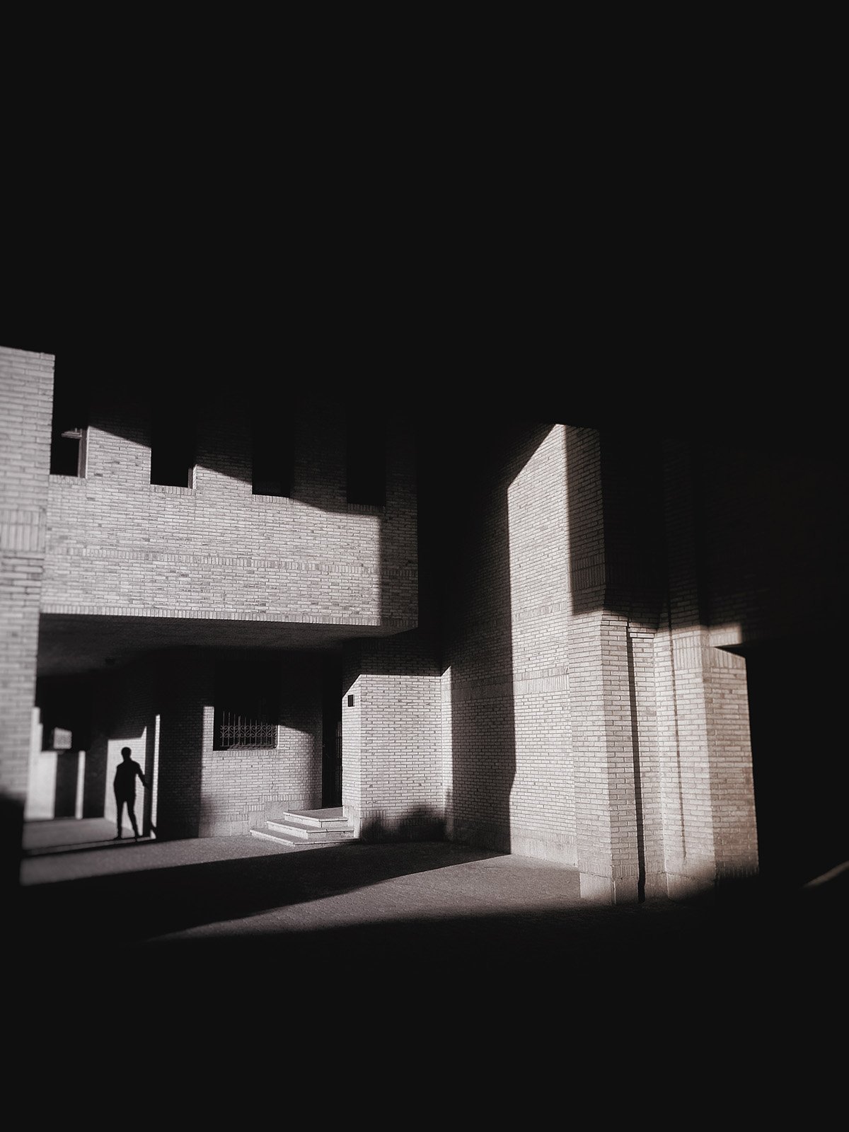 Minimalist street photography from the 'Urban Eclipse' series, featuring silhouettes and sharp geometric shadows against urban brick architecture.
