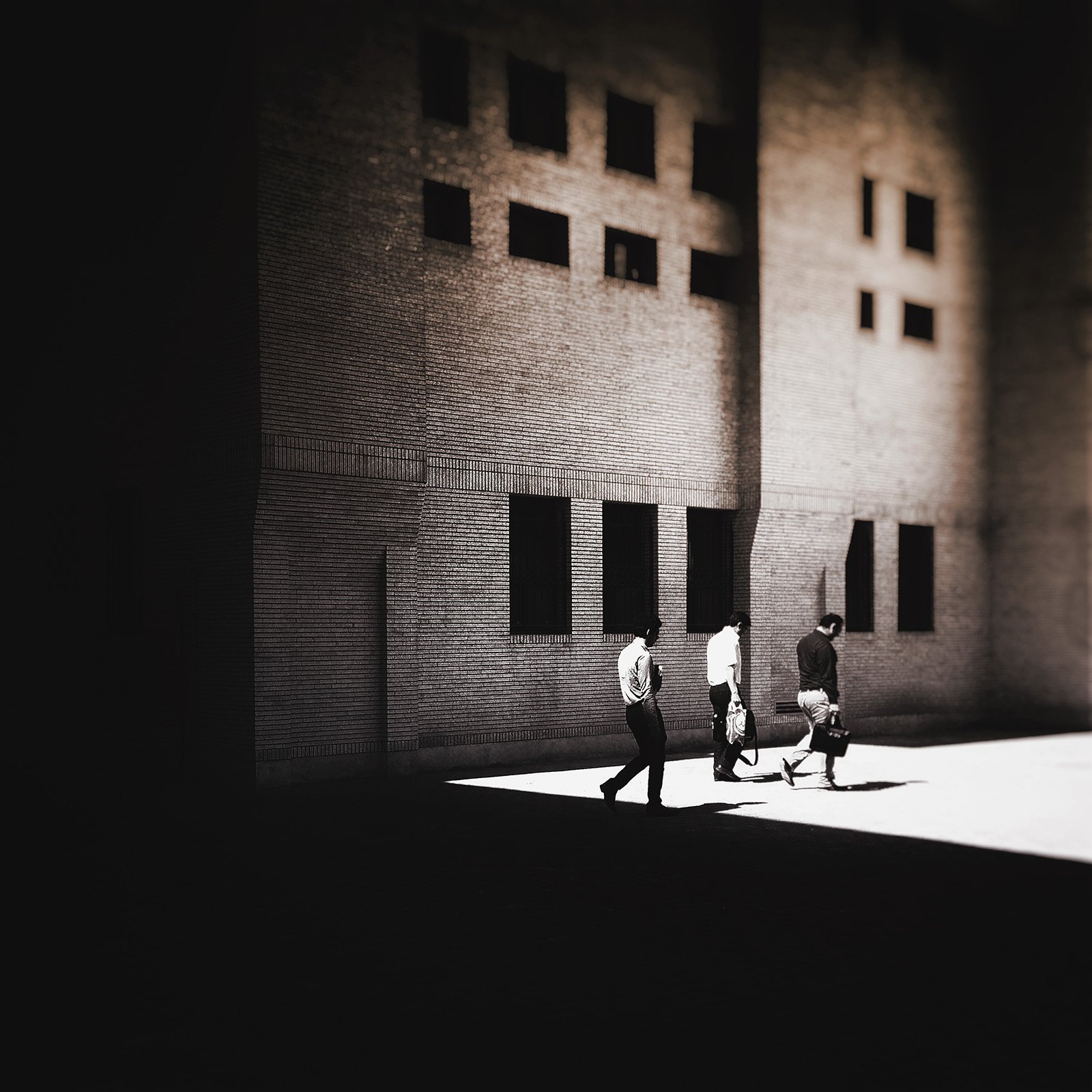 Minimalist street photography from the 'Urban Eclipse' series, featuring silhouettes and sharp geometric shadows against urban brick architecture.