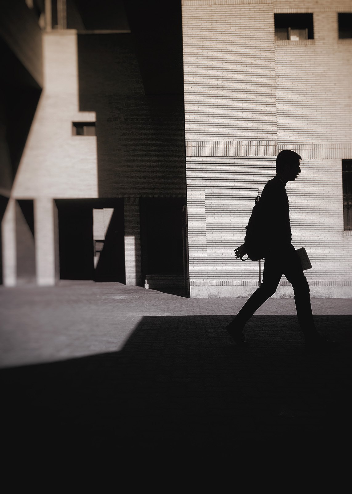 Minimalist street photography from the 'Urban Eclipse' series, featuring silhouettes and sharp geometric shadows against urban brick architecture.