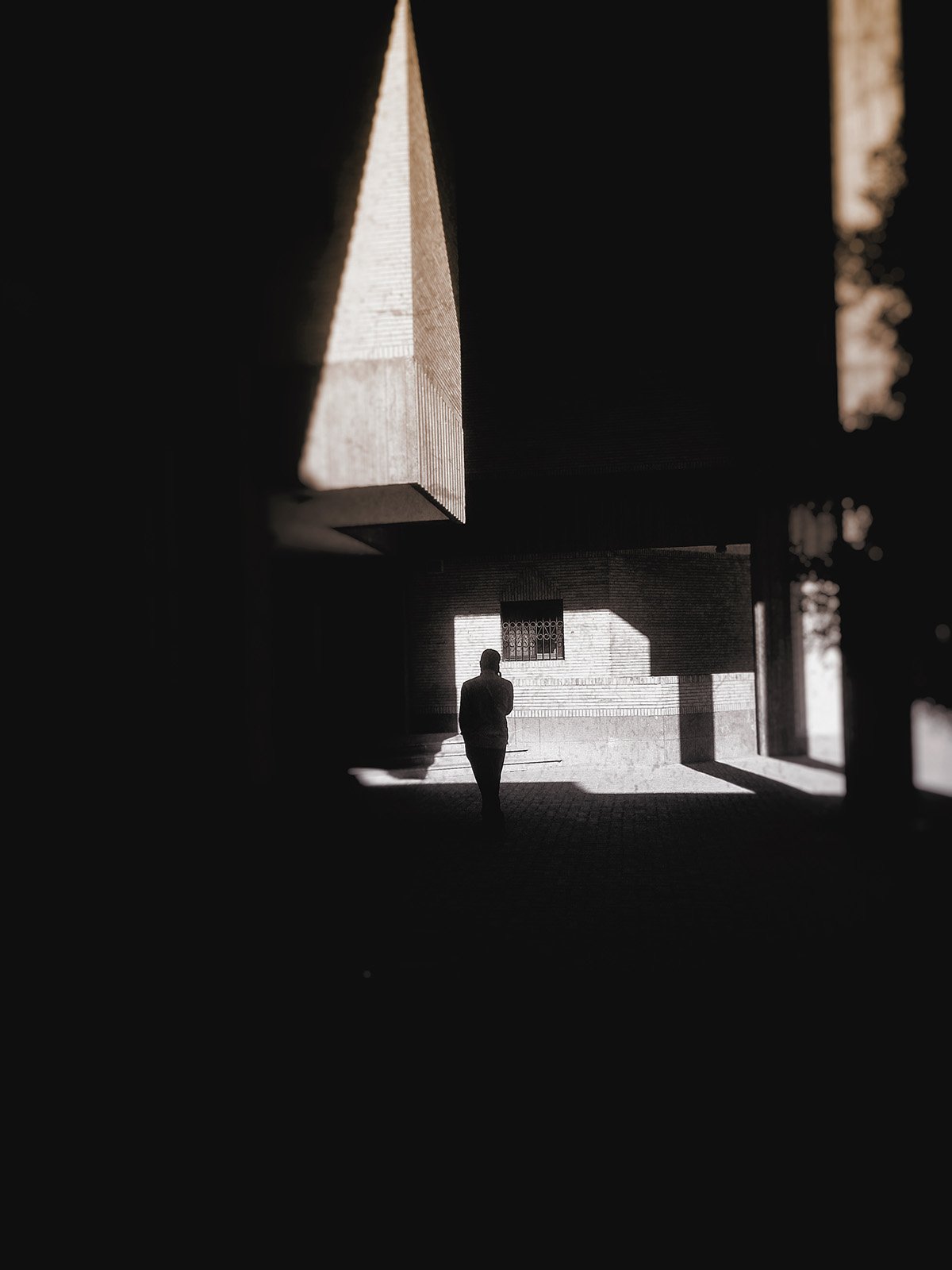 Minimalist street photography from the 'Urban Eclipse' series, featuring silhouettes and sharp geometric shadows against urban brick architecture.