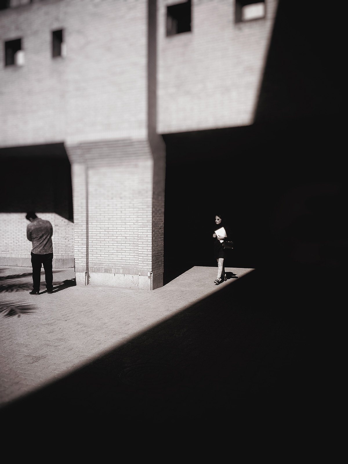Minimalist street photography from the 'Urban Eclipse' series, featuring silhouettes and sharp geometric shadows against urban brick architecture.