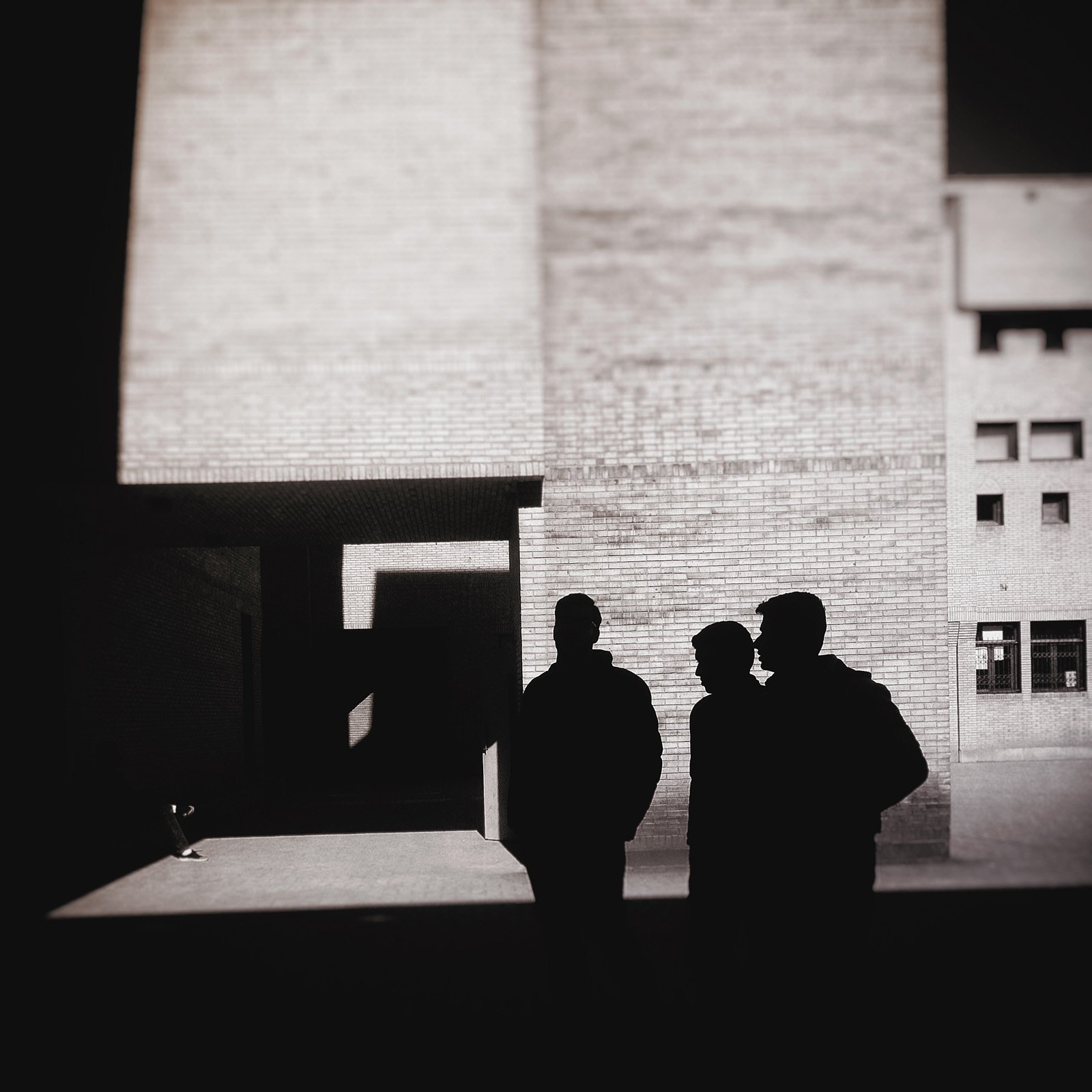Minimalist street photography from the 'Urban Eclipse' series, featuring silhouettes and sharp geometric shadows against urban brick architecture.