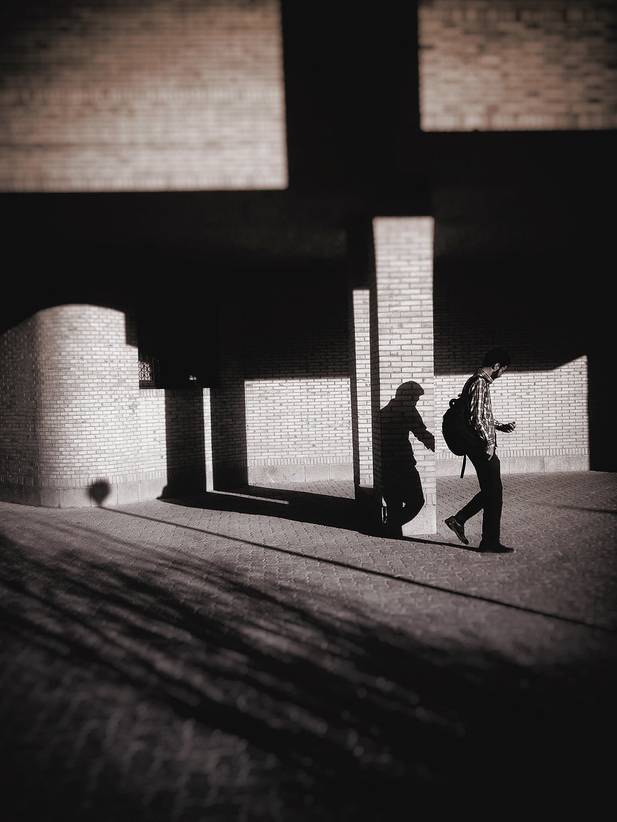 Minimalist street photography from the 'Urban Eclipse' series, featuring silhouettes and sharp geometric shadows against urban brick architecture.