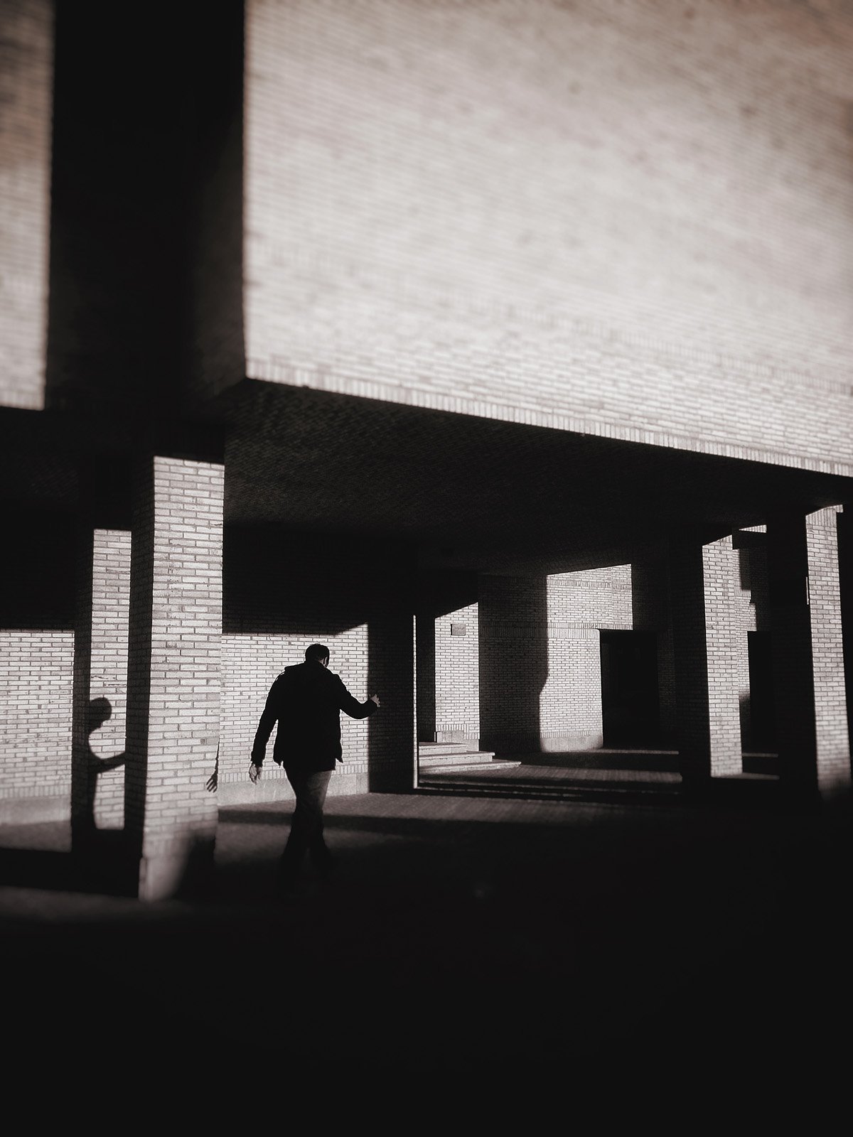 Minimalist street photography from the 'Urban Eclipse' series, featuring silhouettes and sharp geometric shadows against urban brick architecture.