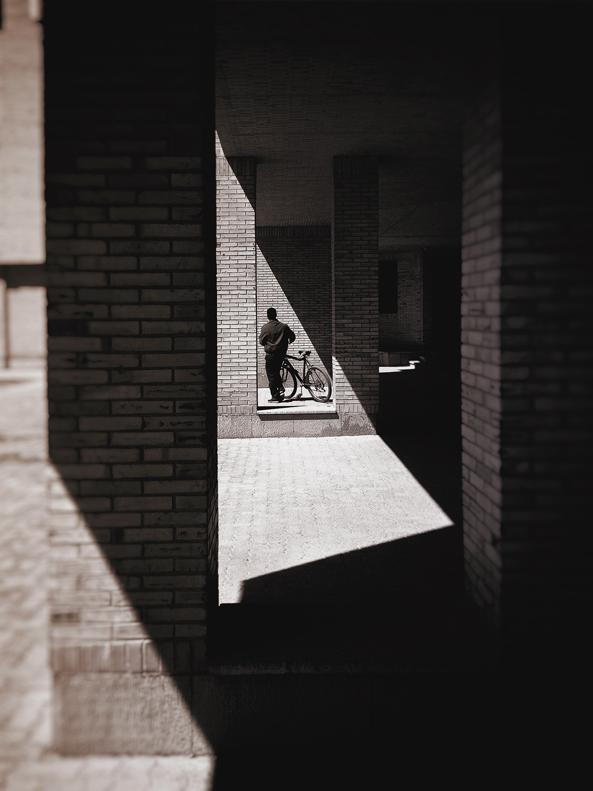 Minimalist street photography from the 'Urban Eclipse' series, featuring silhouettes and sharp geometric shadows against urban brick architecture.
