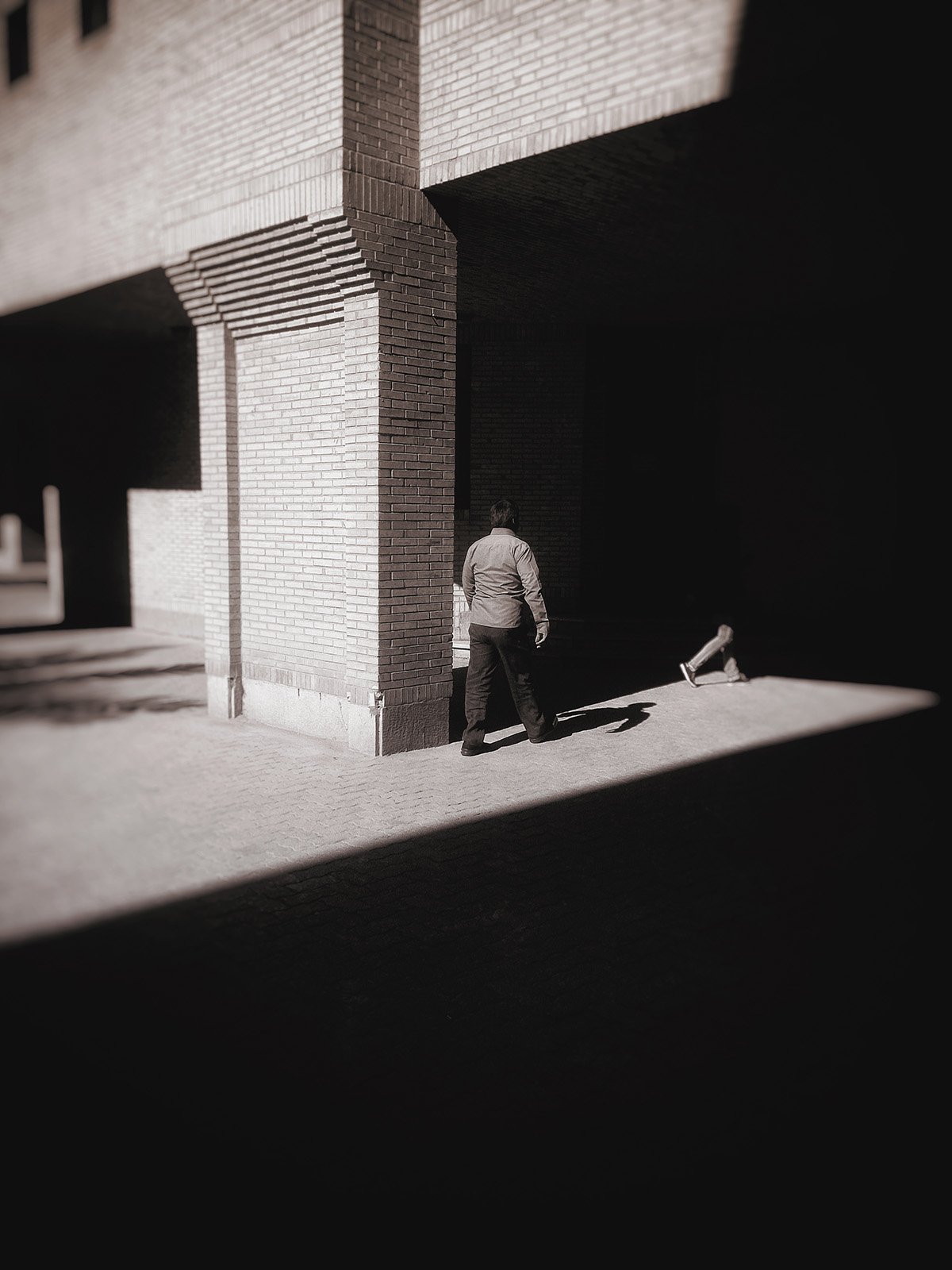 Minimalist street photography from the 'Urban Eclipse' series, featuring silhouettes and sharp geometric shadows against urban brick architecture.