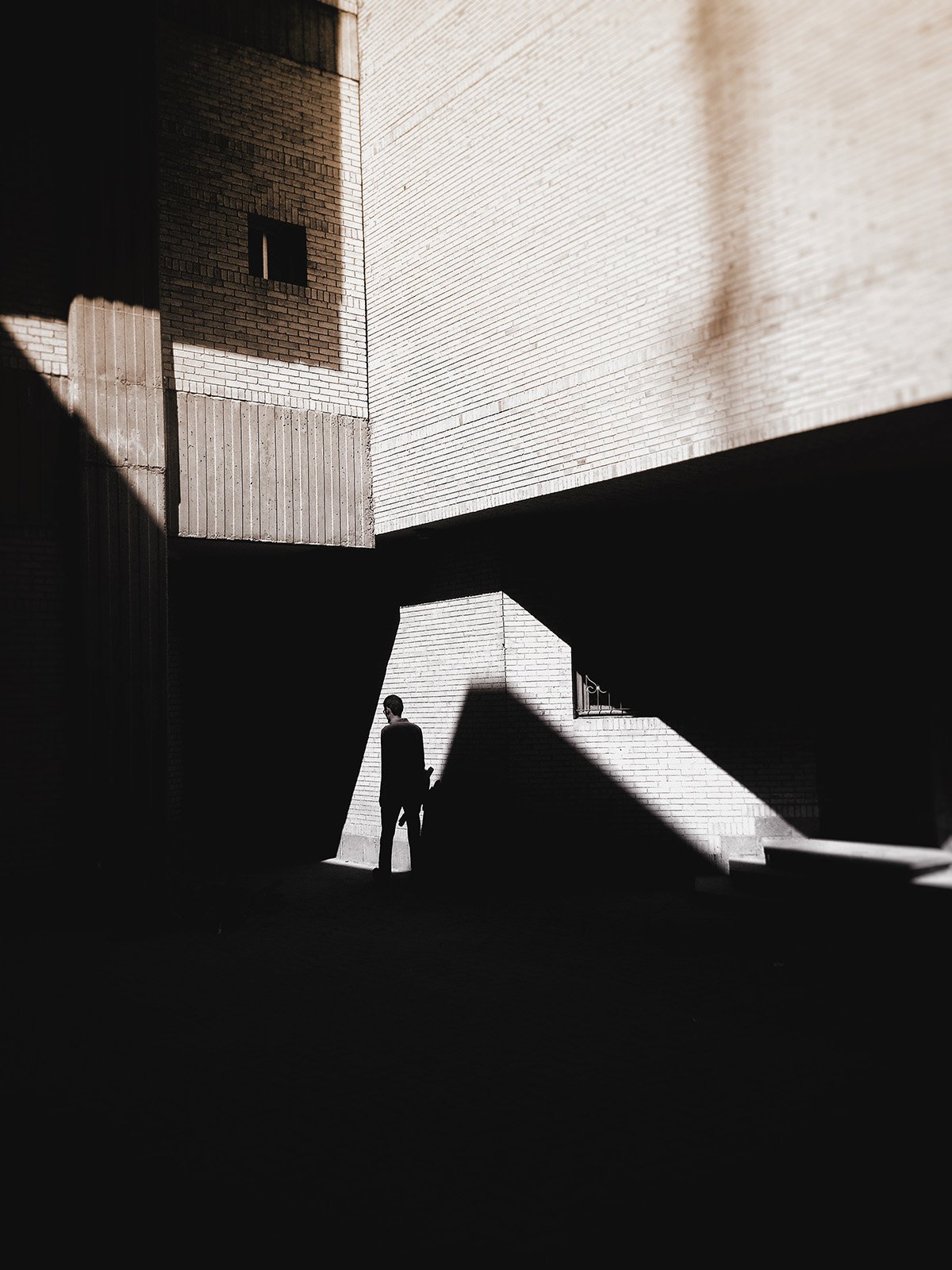 A solitary subject stands at the edge of a geometric shadow, part of a collection focusing on light and shadow in urban environments.