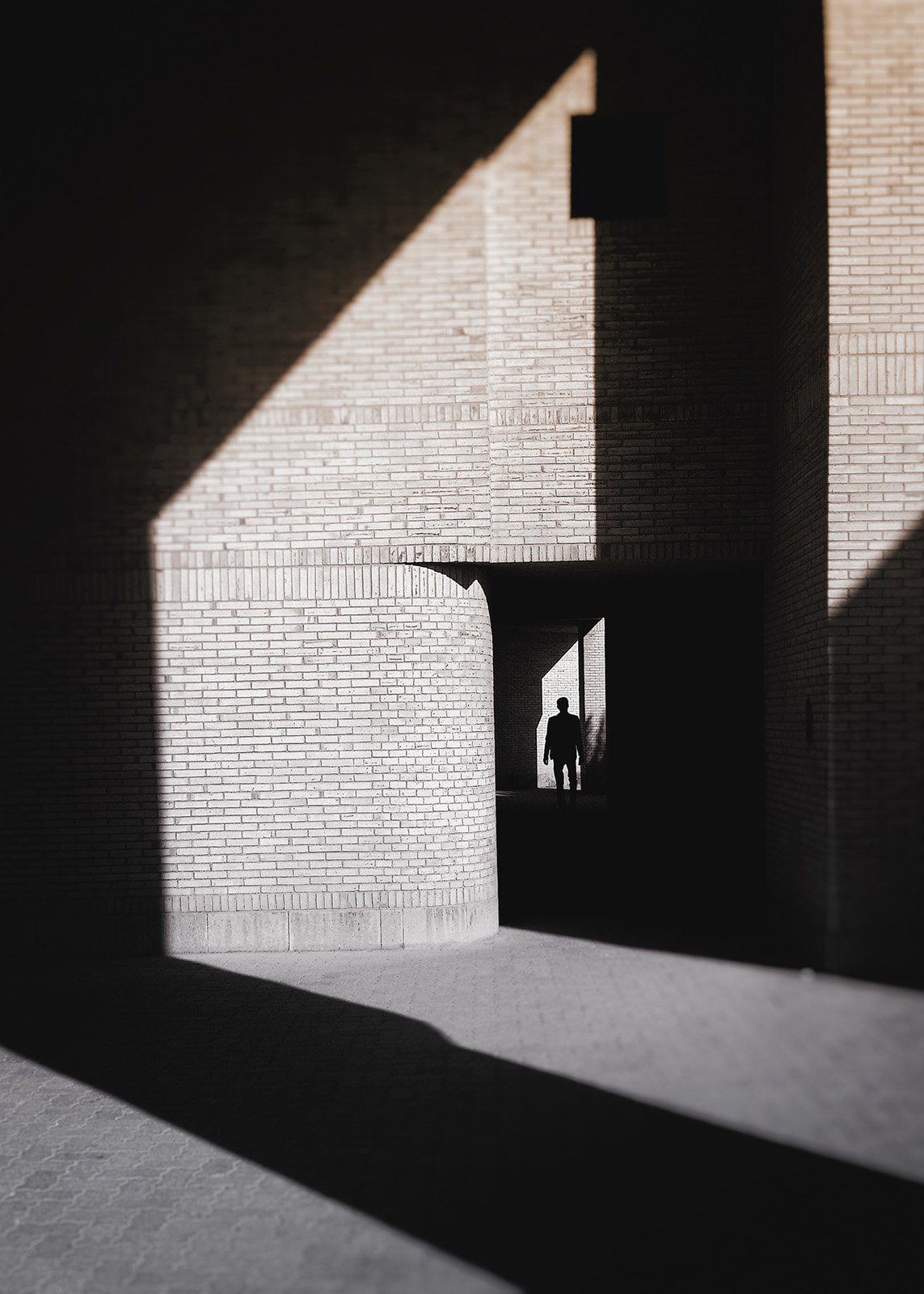 Minimalist street photography from the 'Urban Eclipse' series, featuring silhouettes and sharp geometric shadows against urban brick architecture.