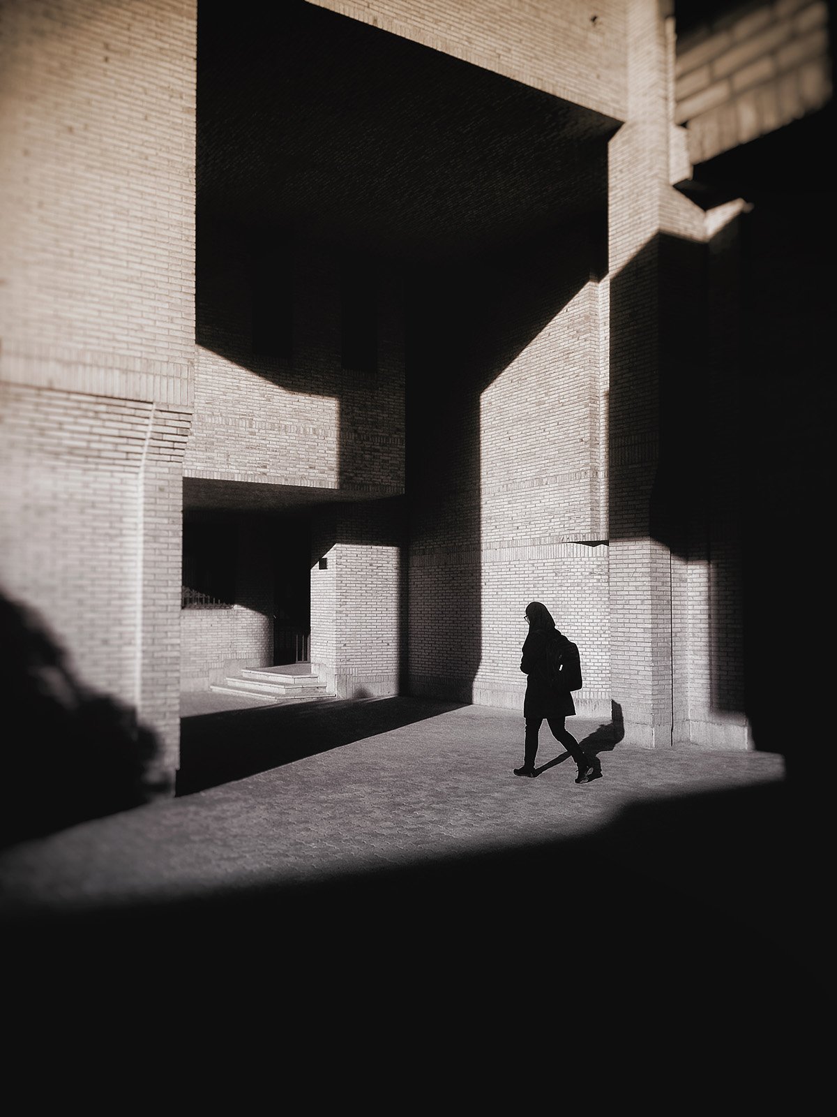 Minimalist street photography from the 'Urban Eclipse' series, featuring silhouettes and sharp geometric shadows against urban brick architecture.