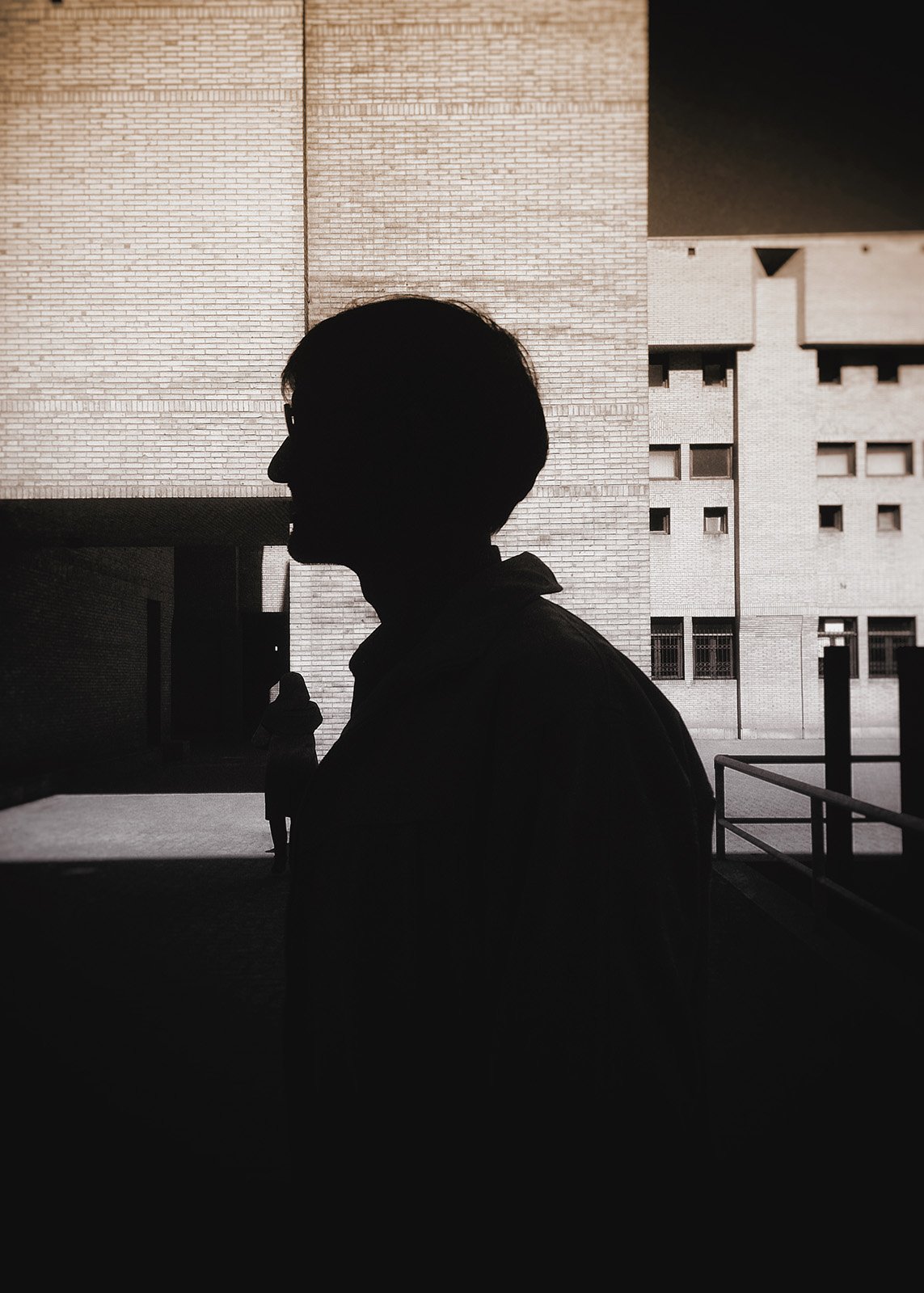 Minimalist street photography from the 'Urban Eclipse' series, featuring silhouettes and sharp geometric shadows against urban brick architecture.