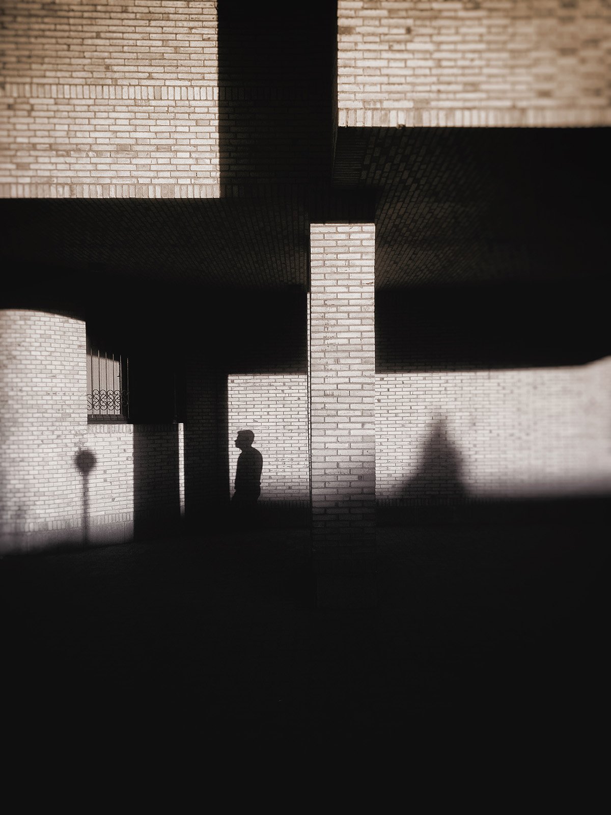 Minimalist street photography from the 'Urban Eclipse' series, featuring silhouettes and sharp geometric shadows against urban brick architecture.