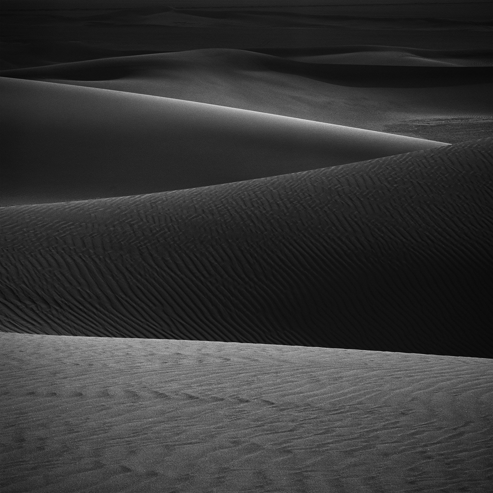 Minimalist photograph of desert sand dunes with soft light, abstract curves, and subtle textures creating a quiet atmospheric composition.