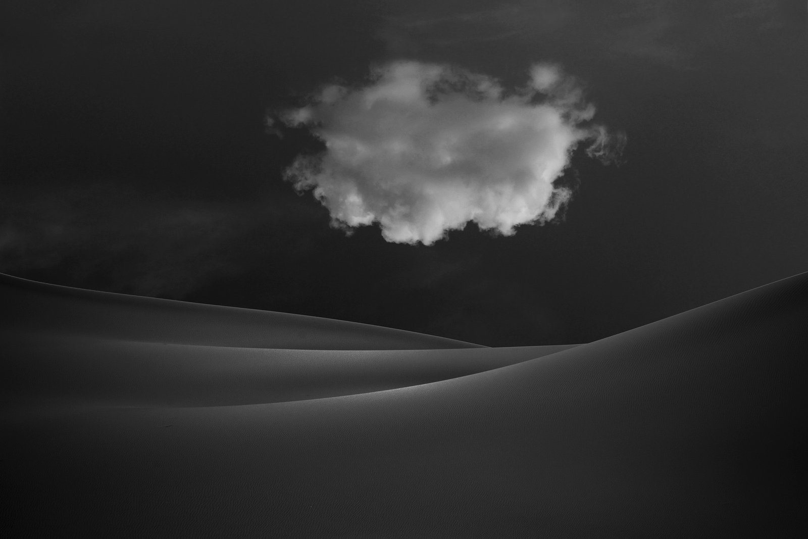 Minimalist photograph of desert sand dunes with soft light, abstract curves, and subtle textures creating a quiet atmospheric composition.