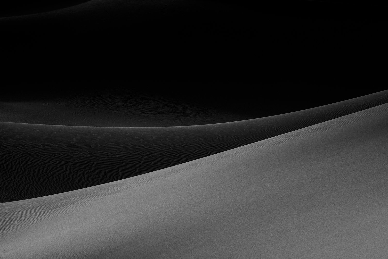 Minimalist photograph of desert sand dunes with soft light, abstract curves, and subtle textures creating a quiet atmospheric composition.